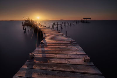 Wooden pier over sea against sky during sunset