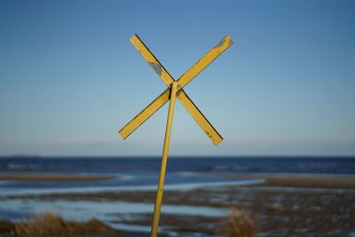 Yellow warning cross at coast for nautical navigation on beach against clear sky