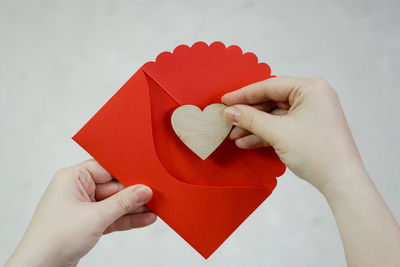 Cropped hand putting heart shape in red envelope