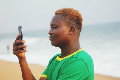 Side view of young man using smart phone at beach