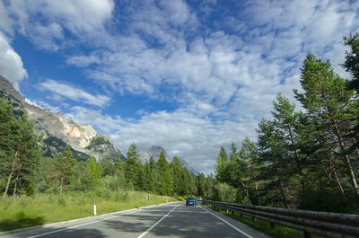 Empty road along trees and plants against sky