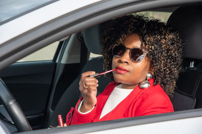 Pretty african american woman in a car doing makeup while standing in a traffic