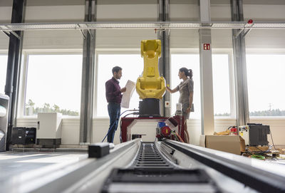 Businessman and woman having a meeting in front of industrial robots in a high tech company