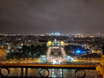 Illuminated bridge over river by buildings against sky at night