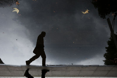 Low angle view of silhouette man reflection on puddle against sky