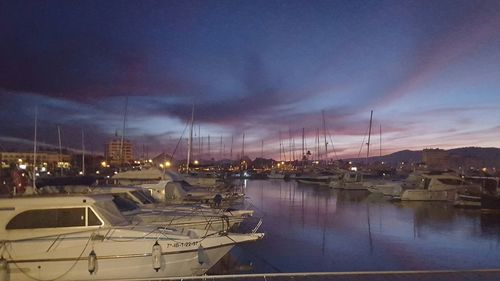 Boats moored in illuminated city against sky at night