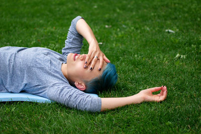 Side view of woman covering eyes while lying on field at park