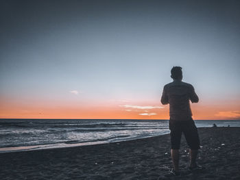 Man standing on beach against sky during sunset