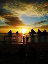 Silhouette people standing on beach against sky during sunset