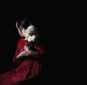 Midsection of woman holding red while sitting against black background