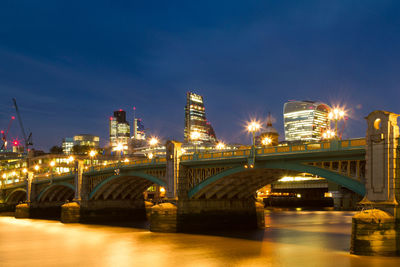 Illuminated bridge over river against sky in city at night