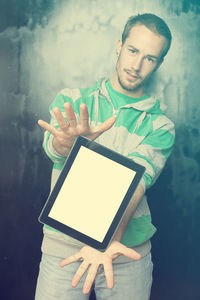 Portrait of young man showing digital tablet while standing against old wall