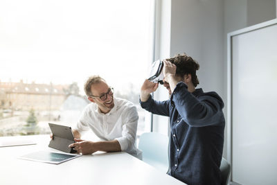 Smiling engineer looking at colleague examining virtual reality simulator in office