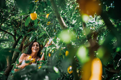 Young woman standing by tree against plants