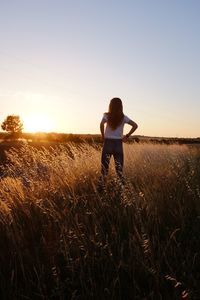 Rear view of teenage girl standing on field against sky during sunset