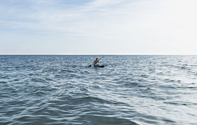 Young woman in distance sitting and paddling on stand up paddle board on blue sea, sup, water sports