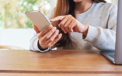 Midsection of woman using mobile phone on table