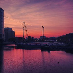 Silhouette of harbor by river against sky during sunset