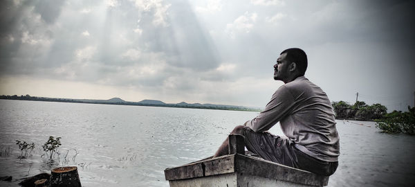 Man sitting by sea against sky
