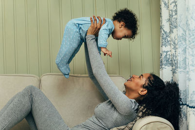 Side view of mother playing with baby boy while lying on sofa at home