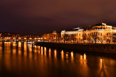 Illuminated buildings by river against sky at night