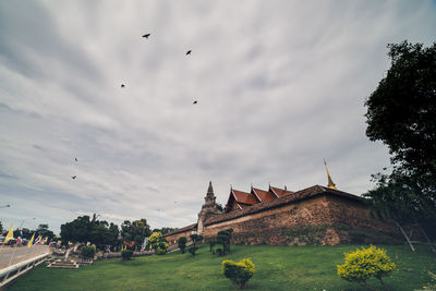 Low angle view of birds flying over temple against cloudy sky