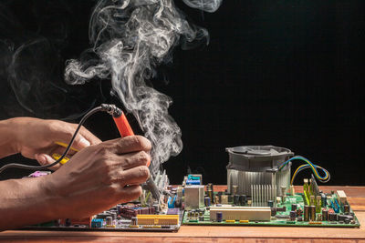 Close-up of man welding motherboard on table against black background