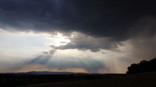 Sunlight streaming through clouds over silhouette landscape