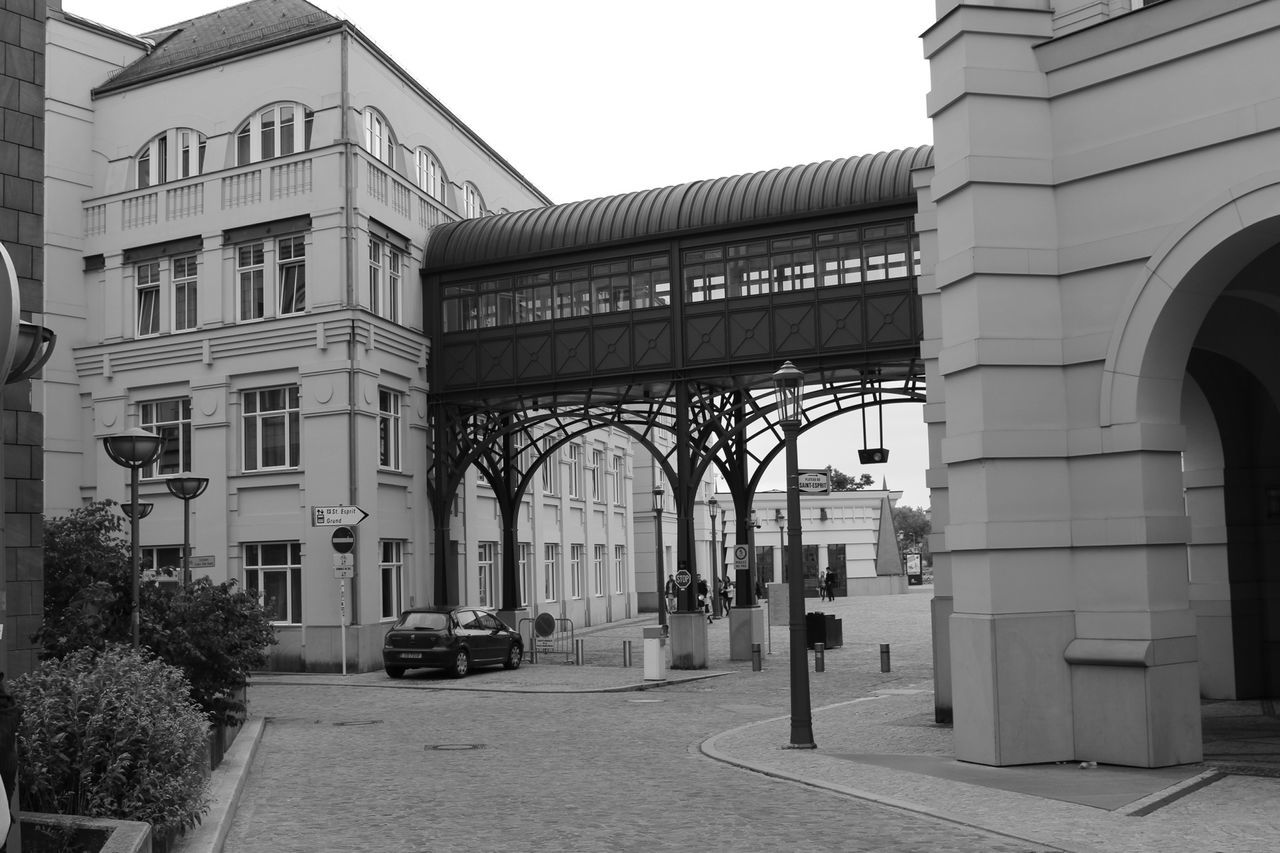 architecture, built structure, building exterior, city, building, arch, street, clear sky, incidental people, transportation, day, window, facade, tree, sky, architectural column, outdoors, car, road, residential building