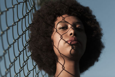 Close-up portrait of woman by chainlink fence against sky