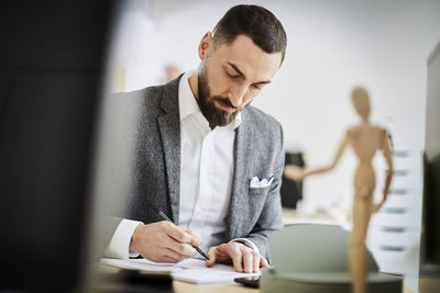 Mid adult businessman writing in note pad at desk in office