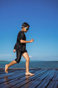 Full length of shirtless boy against sea against clear blue sky