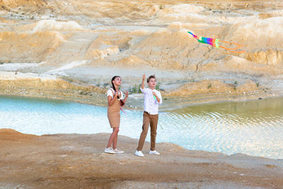 A boy and a girl fly a kite standing on the edge high cliff.
