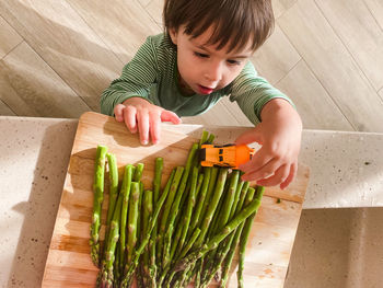 A toddler boy playing with car toy and vegetables in the kitchen