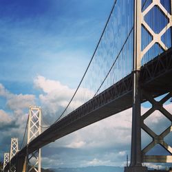 Low angle view of suspension bridge against cloudy sky