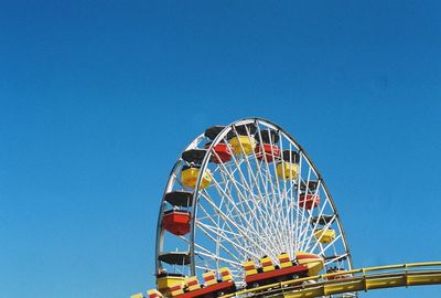 Low angle view of rollercoaster and ferris wheel against clear blue sky