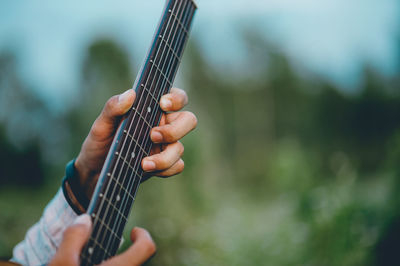 Cropped hands of man playing guitar in park