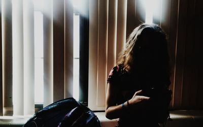 Young woman standing against window blinds