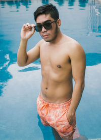 Young shirtless man standing at swimming pool