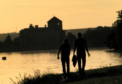 Rear view of silhouette men on water at sunset