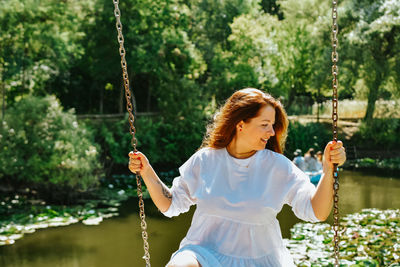 Portrait of young woman swinging against trees