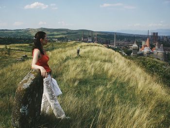 Side view of young woman standing on grassy field against sky