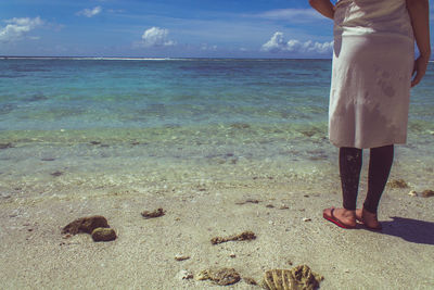 Low section of woman standing on beach against sky