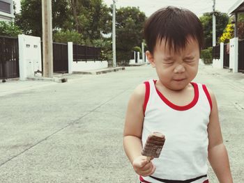 Boy making face while holding ice cream on street in town