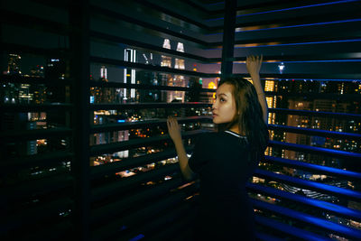 Young woman leaning on window blinds at night