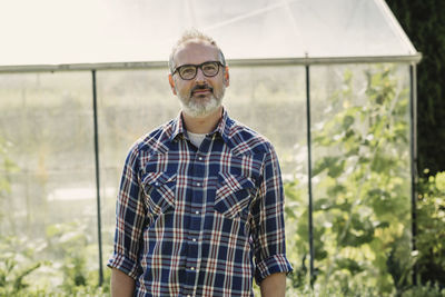 Portrait of mature farmer standing against greenhouse