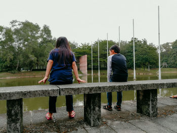 Rear view of girl and boy by lake against sky
