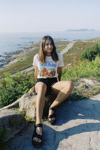 Portrait of young woman sitting on land against sea