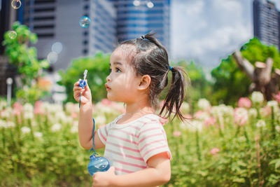 Girl blowing bubbles by flowers at park