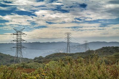 Electricity pylon on mountain against cloudy sky